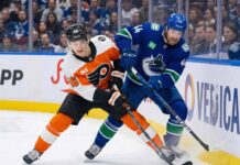 Philadelphia Flyers' Trevor Zegras and Vancouver Canucks' Kiefer Sherwood battle for the puck along the boards during an NHL game.
