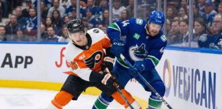 Philadelphia Flyers' Trevor Zegras and Vancouver Canucks' Kiefer Sherwood battle for the puck along the boards during an NHL game.