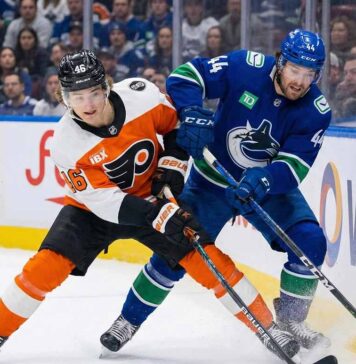 Philadelphia Flyers' Trevor Zegras and Vancouver Canucks' Kiefer Sherwood battle for the puck along the boards during an NHL game.