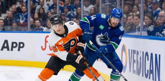 Philadelphia Flyers' Trevor Zegras and Vancouver Canucks' Kiefer Sherwood battle for the puck along the boards during an NHL game.
