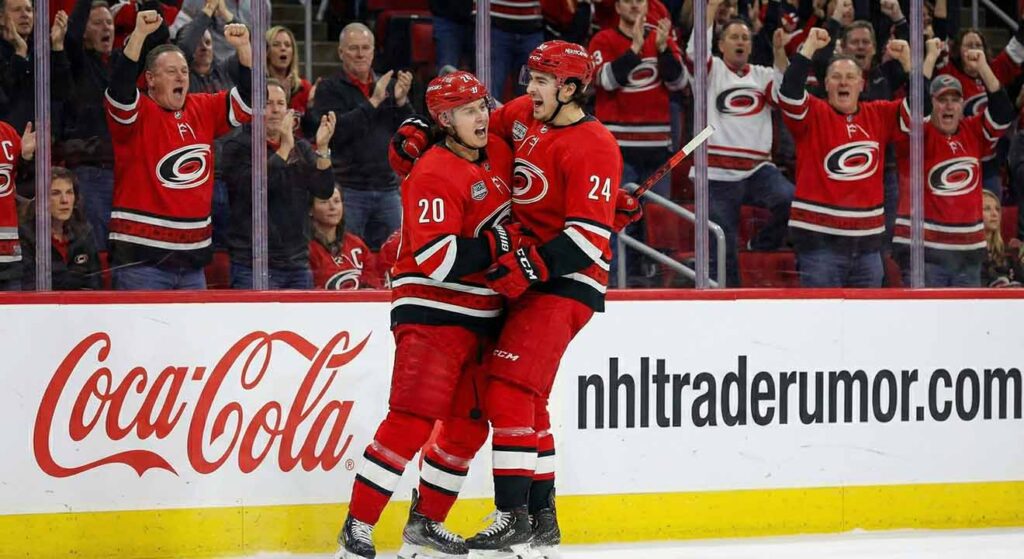 Carolina Hurricanes forwards Sebastian Aho (20) and Seth Jarvis (24) celebrate a goal, embracing in their red home jerseys in front of the boards at PNC Arena.