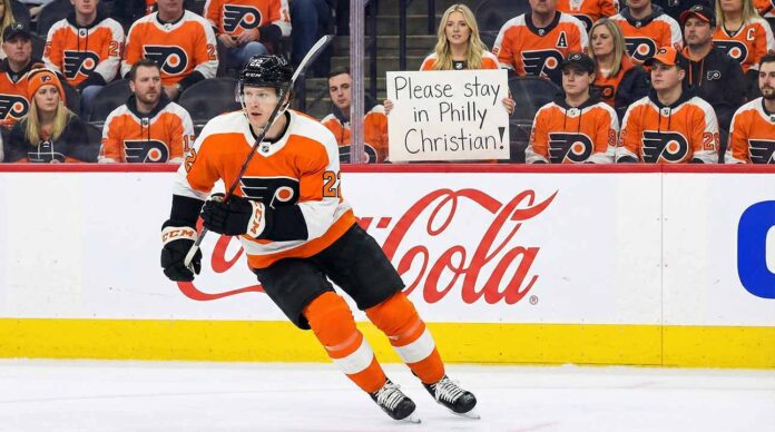 christian-dvorak-philadelphia-flyers-goal-celebration Philadelphia Flyers forward Christian Dvorak (wearing number 22) skating with the puck during an NHL game. In the background stands, a female fan holds up a handwritten sign that reads, "Please stay in Philly Christian!" amid other fans in orange jerseys.