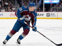 Colorado Avalanche center Ross Colton, wearing number 20 in a burgundy and blue home jersey and a blue helmet, skates across the ice with his stick down during an NHL game.