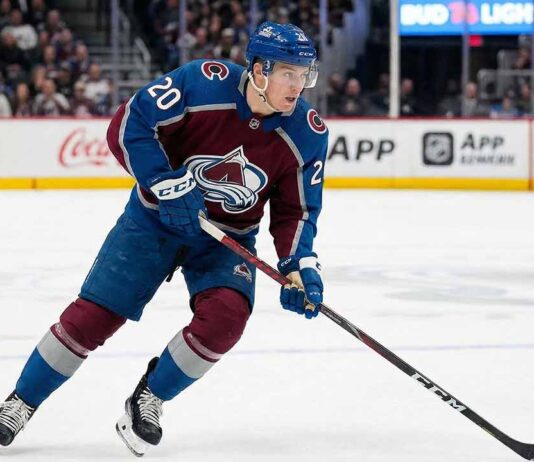 Colorado Avalanche center Ross Colton, wearing number 20 in a burgundy and blue home jersey and a blue helmet, skates across the ice with his stick down during an NHL game.