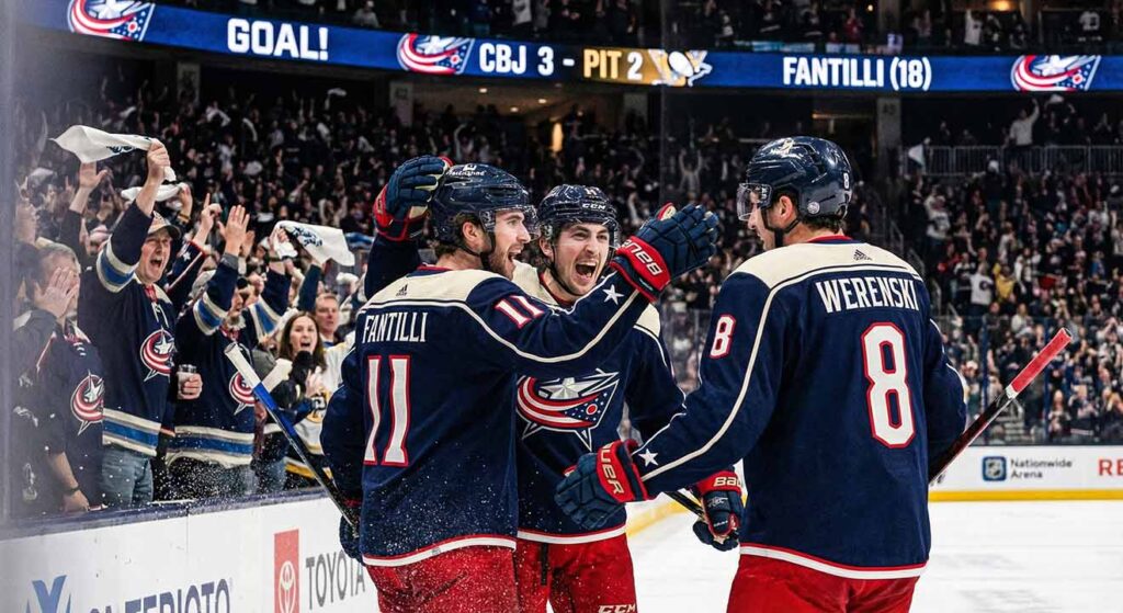 Columbus Blue Jackets players Adam Fantilli (11) and Zach Werenski (8) celebrate a goal with a teammate near the boards during a game against the Pittsburgh Penguins at Nationwide Arena.