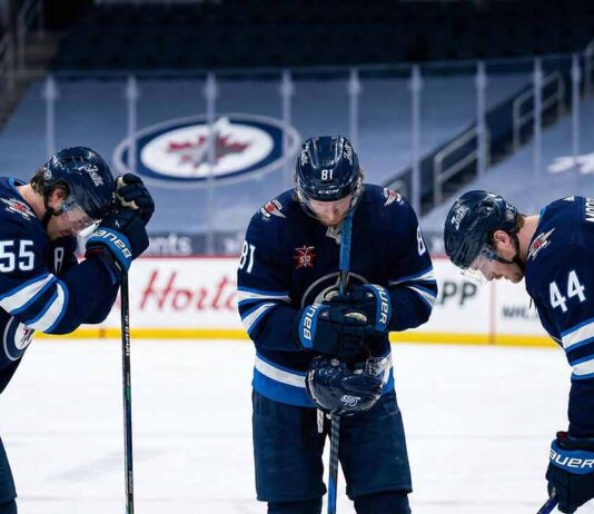Winnipeg Jets players Mark Scheifele (#55), Kyle Connor (#81), and Josh Morrissey (#44) stand dejected on the ice with their heads bowed in frustration inside an empty arena.