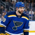 Dillon Dube Is Back: Why The Blues Are Taking A Look Dillon Dube standing on the ice rink wearing a blue St. Louis Blues home uniform and helmet with number 29.