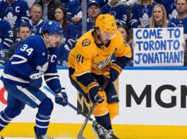 Toronto Maple Leafs captain Auston Matthews battles Nashville Predators forward Jonathan Marchessault for the puck along the boards. A Leafs fan in the background holds up a handmade sign that reads, "COME TO TORONTO JONATHAN!" amidst ongoing trade rumors.