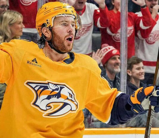 Is Jonathan Marchessault Done in Nashville? 2 Trade Destinations Revealed Jonathan Marchessault of the Nashville Predators, wearing a yellow jersey, celebrates on the ice with his mouth open and stick raised. Behind the glass, fans wearing red Detroit Red Wings apparel cheer.
