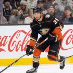 A hockey player, Jordan Kyrou, wearing the black Anaheim Ducks uniform with number 25, is skating with the puck on the ice during a game.