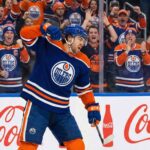 Oilers Rumor Alert: Is Kiefer Sherwood Worth the High Cost? Forward Kiefer Sherwood in a blue Oilers home jersey, yelling and pumping his fist in passionate celebration against the arena glass.