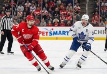 Detroit Red Wings captain Dylan Larkin (#71) skates with the puck through the neutral zone while being pursued by Toronto Maple Leafs captain Auston Matthews (#34) during an NHL game.
