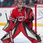 Is Marc-Andre Fleury the Hurricanes’ Stanley Cup Answer? NHL goaltender Marc-Andre Fleury is pictured in full Carolina Hurricanes gear, wearing a red home jersey, customized red and black pads, glove, and blocker, along with a Hurricanes-themed goalie mask. He is in a ready stance within the goal crease during a game environment.