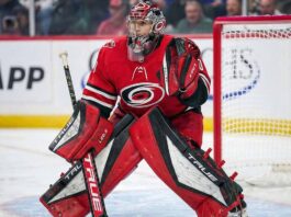 Is Marc-Andre Fleury the Hurricanes’ Stanley Cup Answer? NHL goaltender Marc-Andre Fleury is pictured in full Carolina Hurricanes gear, wearing a red home jersey, customized red and black pads, glove, and blocker, along with a Hurricanes-themed goalie mask. He is in a ready stance within the goal crease during a game environment.