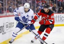 Toronto Maple Leafs' John Tavares (91) and New Jersey Devils' Jack Hughes (86) battle fiercely for possession of the puck along the boards during an NHL game.