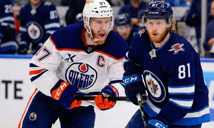 oilers-vs-jets-dec-29-2025-preview Edmonton Oilers captain Connor McDavid (#97) in a white away jersey yelling while skating intensely alongside Winnipeg Jets forward Kyle Connor (#81) in a dark blue home jersey during an NHL game.