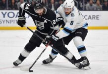 Los Angeles Kings center Phillip Danault (24), wearing a black home jersey, battles intensely for the puck along the ice with Utah forward Nick Schmaltz (8), wearing a white away jersey, during an NHL game.