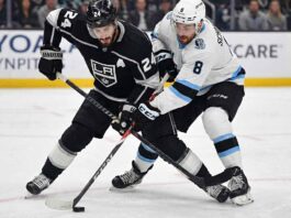 Los Angeles Kings center Phillip Danault (24), wearing a black home jersey, battles intensely for the puck along the ice with Utah forward Nick Schmaltz (8), wearing a white away jersey, during an NHL game.