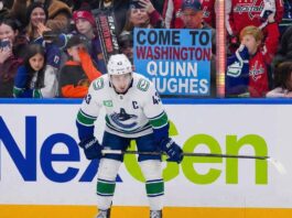 Why the Canucks Might Actually Trade Quinn Hughes to the Capitals Vancouver Canucks captain Quinn Hughes stands on the ice in his away jersey, looking towards the boards where a fan holds a sign that reads 'Come to Washington Quinn Hughes'.