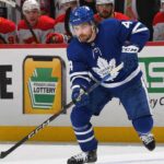 Toronto Maple Leafs defenseman Rasmus Andersson (#4) is pictured skating with the puck during a game, wearing the team's blue home jersey featuring the large white Maple Leaf crest, blue helmet, and blue gloves.