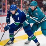 Vancouver Canucks forward Brock Boeser (#6) and San Jose Sharks forward Macklin Celebrini (#71) battle for the puck along the boards during an NHL game.