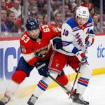 Florida Panthers forward Brad Marchand (63) and New York Rangers forward Artemi Panarin (10) battle fiercely for possession of the puck along the boards during an NHL game.