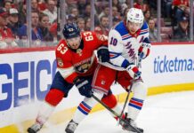 Florida Panthers forward Brad Marchand (63) and New York Rangers forward Artemi Panarin (10) battle fiercely for possession of the puck along the boards during an NHL game.