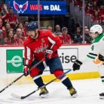 Washington Capitals captain Alex Ovechkin (8) skates with the puck while being defended by Dallas Stars defenseman Miro Heiskanen (4) during an NHL game at Capital One Arena. Fans fill the stands and a scoreboard reads "WAS vs DAL" in the background.