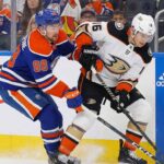 Edmonton Oilers forward Andrew Mangiapane (88) in a blue home jersey and Anaheim Ducks center Ryan Strome (16) in a white away jersey battle for possession of the puck along the rink boards during an NHL game.