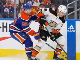 Edmonton Oilers forward Andrew Mangiapane (88) in a blue home jersey and Anaheim Ducks center Ryan Strome (16) in a white away jersey battle for possession of the puck along the rink boards during an NHL game.