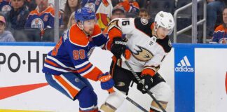 Edmonton Oilers forward Andrew Mangiapane (88) in a blue home jersey and Anaheim Ducks center Ryan Strome (16) in a white away jersey battle for possession of the puck along the rink boards during an NHL game.
