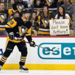 Pittsburgh Penguins forward Anthony Mantha (#39) skates on the ice near the boards. Behind the protective glass, fans cheer, and a woman in the front row holds up a handwritten white sign that reads, "Please don't leave Anthony!".
