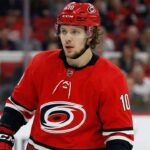 The Breadman in Raleigh? Why the Hurricanes are the Ultimate Wildcard for an Artemi Panarin Trade A close-up photograph of NHL forward Artemi Panarin wearing a red Carolina Hurricanes home jersey with the number 10 and a matching red helmet, looking towards the left side of the rink during a game.
