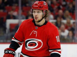 The Breadman in Raleigh? Why the Hurricanes are the Ultimate Wildcard for an Artemi Panarin Trade A close-up photograph of NHL forward Artemi Panarin wearing a red Carolina Hurricanes home jersey with the number 10 and a matching red helmet, looking towards the left side of the rink during a game.