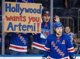 Panarin to Kings? Why This Trade Rumor Changes Everything A New York Rangers fan behind the glass holds up a cardboard sign that reads "Hollywood wants you Artemi!" as Rangers forward Artemi Panarin skates on the ice during a game, highlighting trade rumors linking him to the Los Angeles Kings.