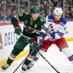 Minnesota Wild forward Kirill Kaprizov (green jersey, #97) and New York Rangers forward Artemi Panarin (white jersey, #10) battle for the puck along the boards during an NHL game.