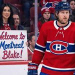 A photo of NHL player Blake Coleman on the ice, wearing a red Montreal Canadiens jersey with number 20 and a blue helmet. Behind the glass boards, a woman with dark hair is holding a handwritten white sign with red and blue script that reads "Welcome to Montreal Blake!". Other fans are visible in the background.