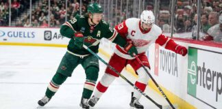 Minnesota Wild's Kirill Kaprizov (#97 in green jersey) and Detroit Red Wings' Dylan Larkin (#71 in white jersey) battle for possession of the puck against the rink boards during an NHL game.