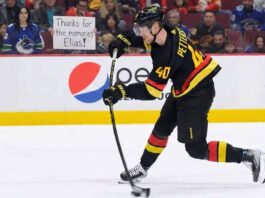 Elias Pettersson (#40) of the Vancouver Canucks, wearing his black "Flying V" jersey, winds up for a slapshot on the ice. Behind him, a female fan with dark hair stands in the front row behind the glass, holding a white sign with handwritten black text that reads, "Thanks for the memories Elias!". Other fans fill the red seats in the background.