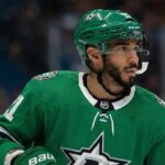 Is Evander Kane the Missing Piece for the Dallas Stars’ Cup Run? Close-up photograph of NHL player Evander Kane on the ice, wearing a green Dallas Stars home jersey with the number 91 visible on the sleeve, a green Stars helmet, and gloves. He is looking toward the right side of the frame with a white mouthguard hanging from his mouth. Blurred spectators fill the background stands.