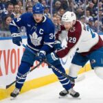 Toronto Maple Leafs captain Auston Matthews (34) and Colorado Avalanche forward Nathan MacKinnon (29) battle fiercely for the puck against the sideboards during an NHL game at Scotiabank Arena.