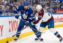 Toronto Maple Leafs captain Auston Matthews (34) and Colorado Avalanche forward Nathan MacKinnon (29) battle fiercely for the puck against the sideboards during an NHL game at Scotiabank Arena.