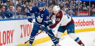 Toronto Maple Leafs captain Auston Matthews (34) and Colorado Avalanche forward Nathan MacKinnon (29) battle fiercely for the puck against the sideboards during an NHL game at Scotiabank Arena.