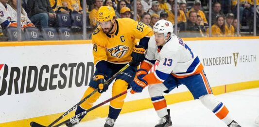 Islanders vs Predators Viewing Guide: Will NY Stay Hot in Nashville? Nashville Predators captain Roman Josi (#59) in a yellow jersey and New York Islanders forward Mathew Barzal (#13) in a white jersey battle for the puck along the boards during an NHL game at Bridgestone Arena.