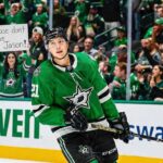 Dallas Stars forward Jason Robertson (#21) skates on the ice, looking towards a female fan behind the rink glass holding a handwritten sign that reads "Please don't leave Jason!".