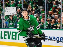 Dallas Stars forward Jason Robertson (#21) skates on the ice, looking towards a female fan behind the rink glass holding a handwritten sign that reads "Please don't leave Jason!".