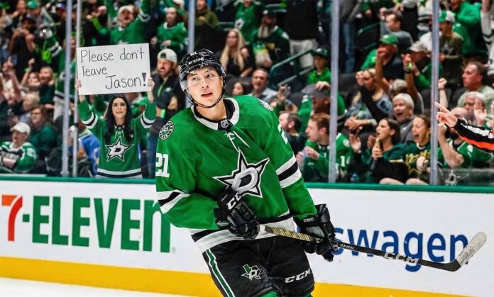 Dallas Stars forward Jason Robertson (#21) skates on the ice, looking towards a female fan behind the rink glass holding a handwritten sign that reads "Please don't leave Jason!".