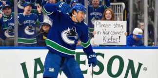 Vancouver Canucks forward Kiefer Sherwood celebrates a goal on the ice, with a female fan behind the glass holding a sign that reads "Please stay in Vancouver Kiefer!". The Jameson ad is visible on the boards.