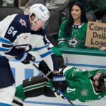 Why the Winnipeg Jets Must Trade Logan Stanley Now A smiling female Dallas Stars fan in the stands holds a cardboard sign reading "Come to Dallas Logan!" while Winnipeg Jets defenseman Logan Stanley checks a Stars player into the boards just in front of her behind the glass.