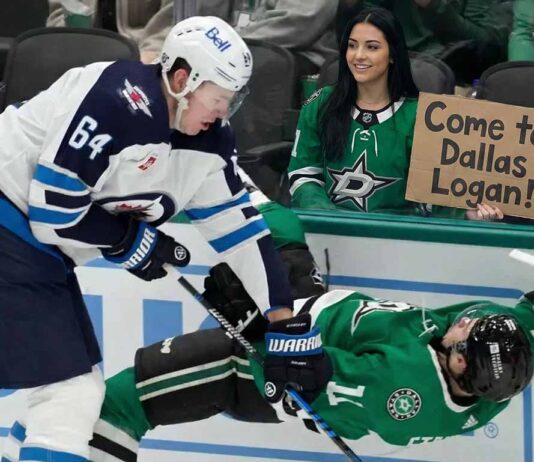 Why the Winnipeg Jets Must Trade Logan Stanley Now A smiling female Dallas Stars fan in the stands holds a cardboard sign reading "Come to Dallas Logan!" while Winnipeg Jets defenseman Logan Stanley checks a Stars player into the boards just in front of her behind the glass.